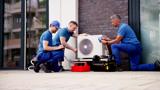Three men working on an external air conditioning unit.