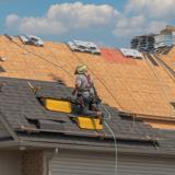 A man, crouched, doing work on a triangular roof.