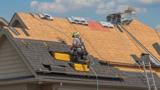 A man, crouched, doing work on a triangular roof.